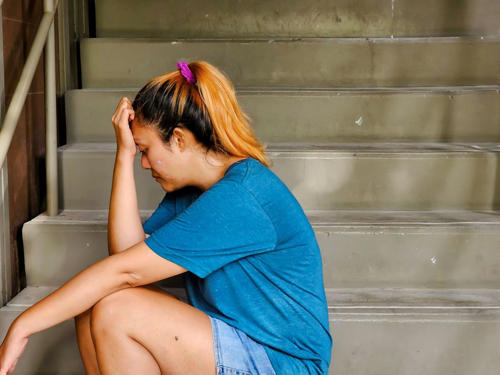 Southeast Asian woman sitting alone on a stairwell with her hand touching her forehead looking depressed