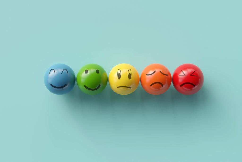 5 colourful balls on a sky blue background with different emotions on on them. They are each indicating a different emotion: very happy, contentment, discouragement, sadness, anger