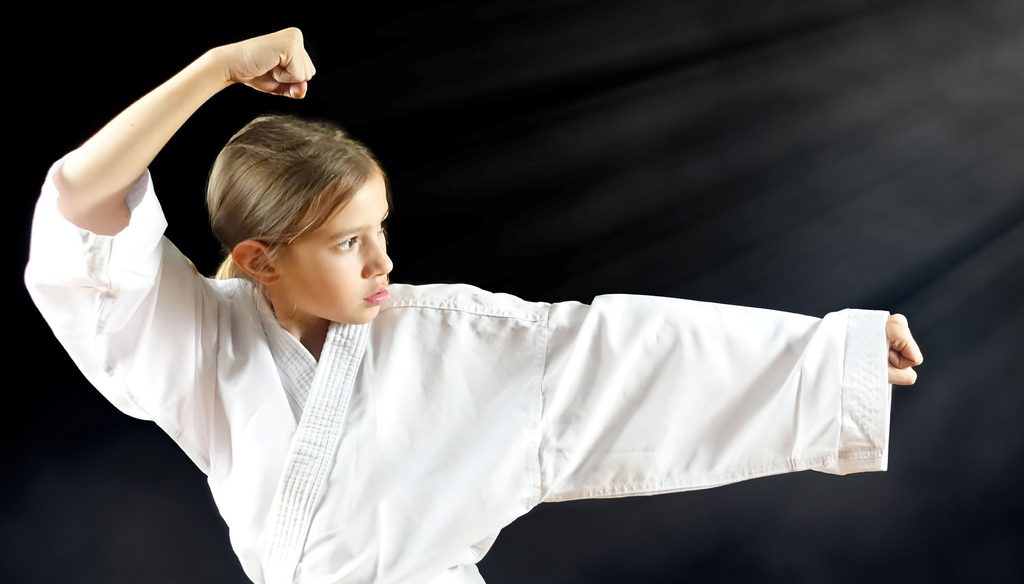 White teenage girl in a martial arts uniform punching air attack fight pose.